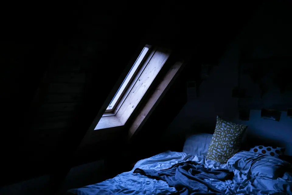 Een slaapkamer in de nacht, met een dakraam waardoor maanlicht op het dekbed valt