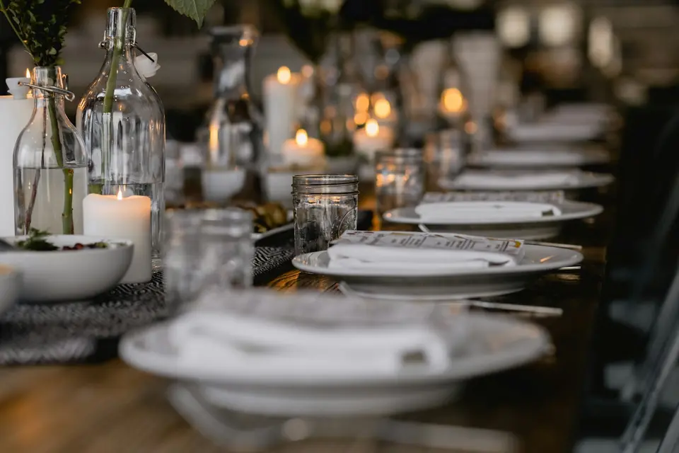 Een lange gedekte tafel met witte borden, glazen en brandende kaarsen