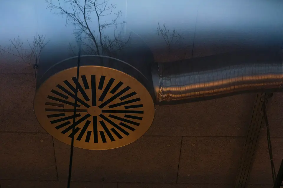 Een rond metalen ventilatierooster met een kanaal ernaast, onder een plafond