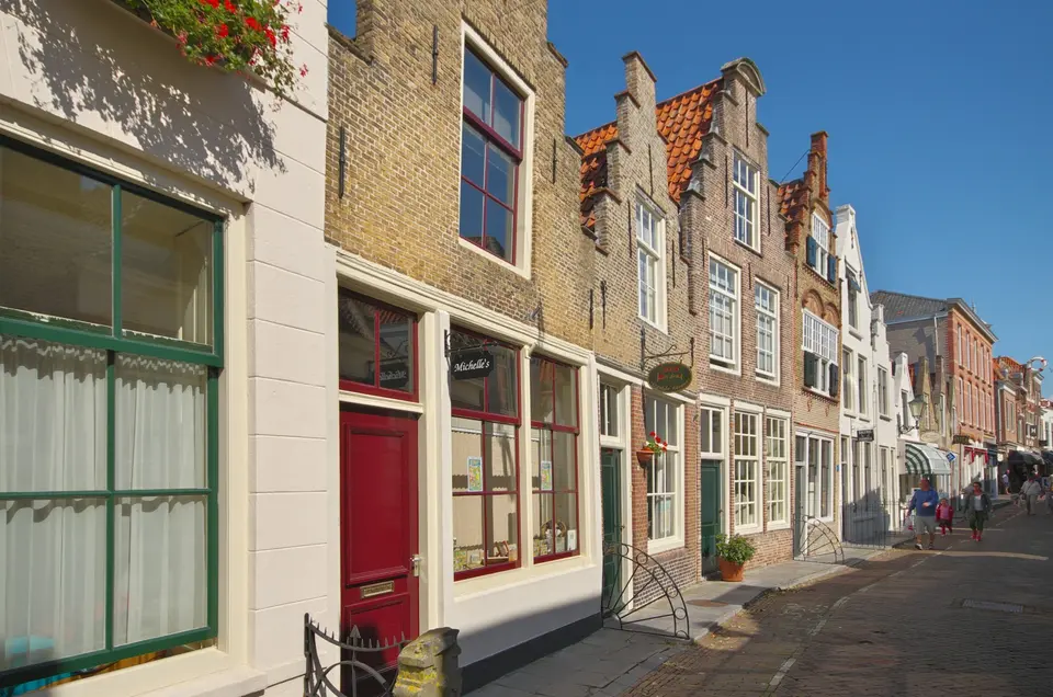 Een straat met bakstenen huizen, groene kozijnen en een stoep van klinkers